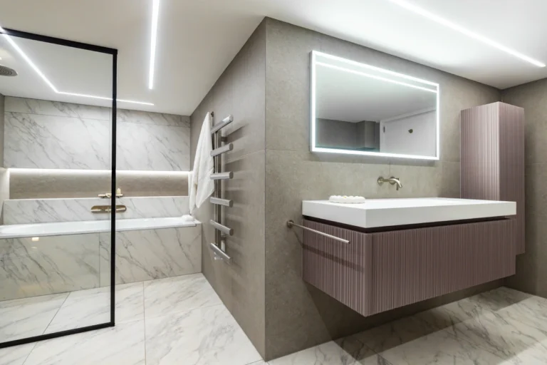 Modern bathroom with marble tiles, floating vanity, and illuminated mirror.
