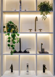 Modern bathroom fixtures with black and gold taps on illuminated shelves with plants.