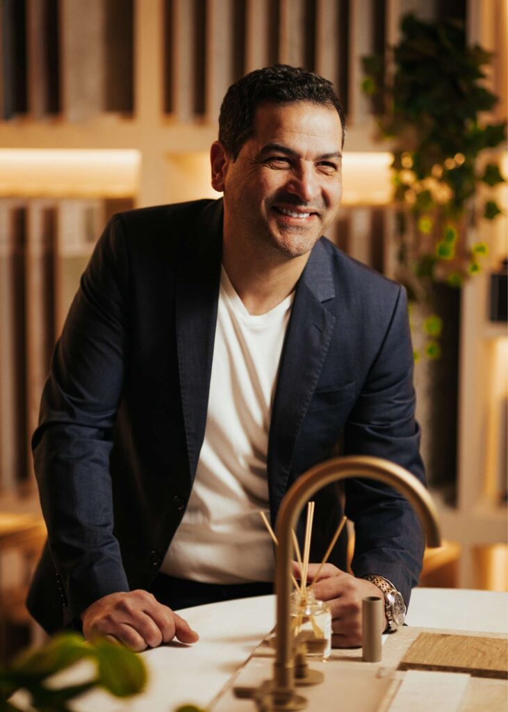 Smiling man in a modern kitchen with wooden accents and greenery.