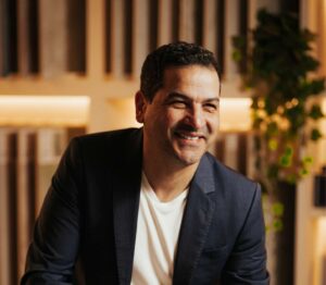 Smiling man in a modern kitchen with wooden accents and greenery.