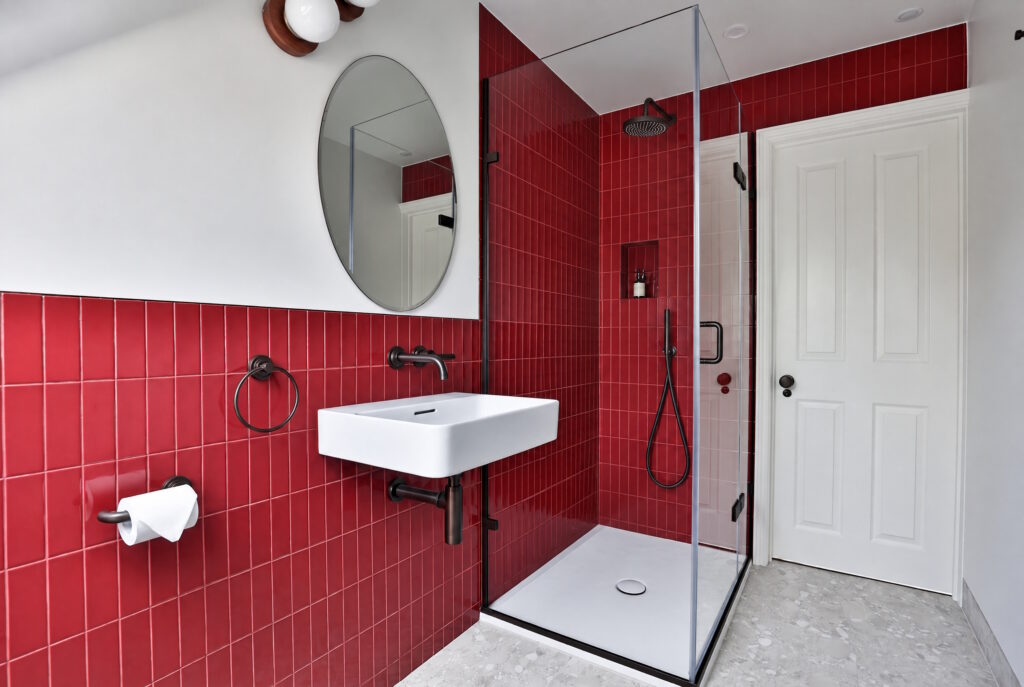 Modern bathroom with red tiled shower area and white sink.