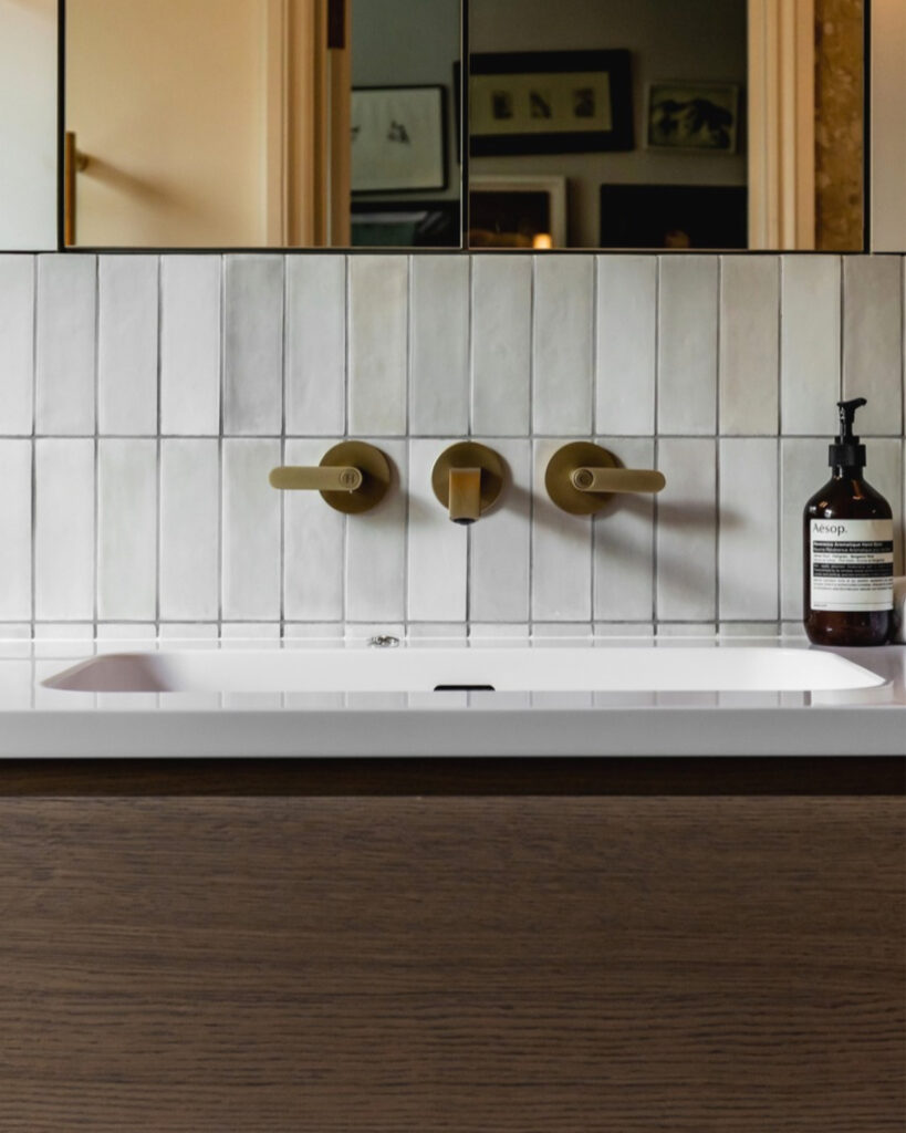 Modern bathroom sink with gold fixtures and white tiled wall in Victorian home.