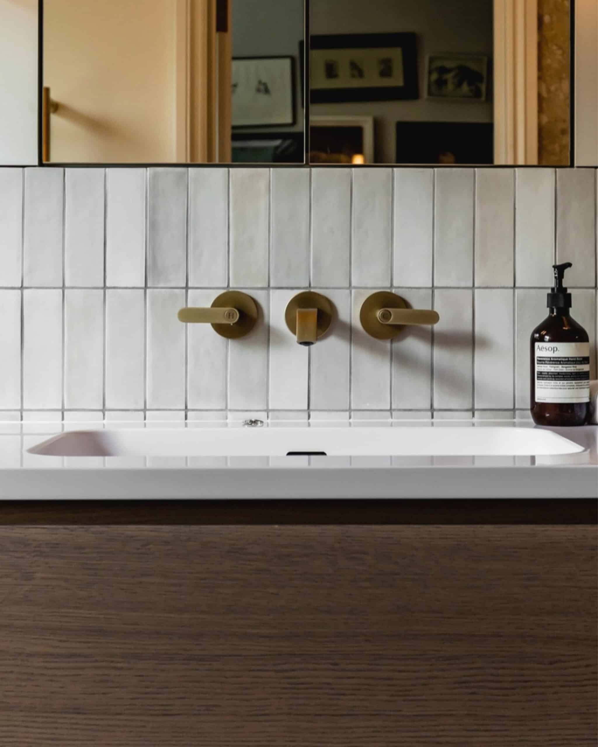 Modern bathroom sink with gold fixtures and white tiled wall in Victorian home.