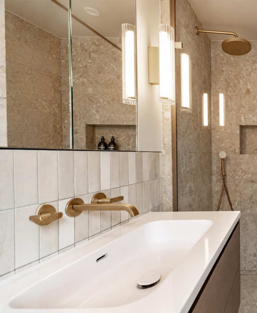 Modern bathroom with beige tiles, gold fixtures, and a white sink.
