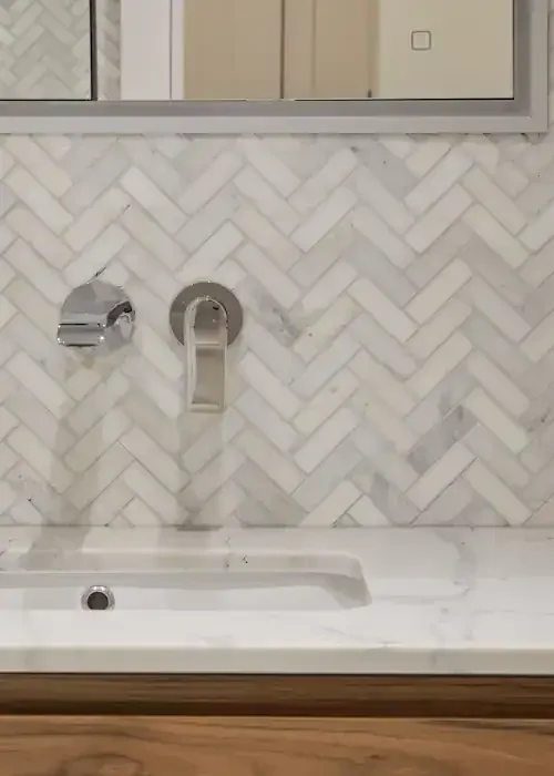 Elegant herringbone tile backsplash behind bathroom sink with chrome fixtures.