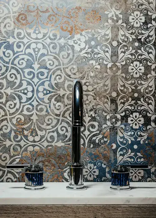 Modern chrome bathroom tap with dual handles against decorative patterned tiles.