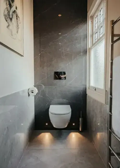 Modern wall-hung toilet in a sleek bathroom with grey marble tiles and natural light.