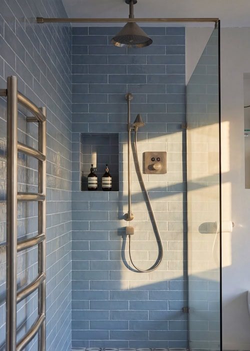 Blue tiled walk-in shower with rain shower head and handheld shower attachment.