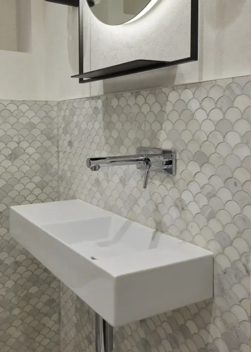 Wall-mounted bathroom sink with mirror and hexagonal tile wall in modern bathroom.
