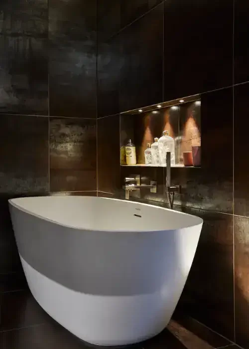 Freestanding bathtub in a contemporary bathroom with dark wall tiles and ambient lighting.