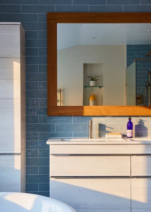 Modern bathroom vanity with sleek white cabinet and large mirror, blue tiled wall, and stylish acces.