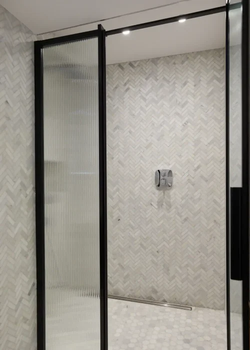 Walk-in shower with black-framed glass door and textured wall tiles.