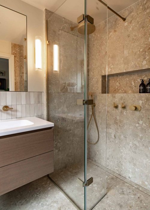Modern walk-in shower with glass enclosure and beige stone tiles.