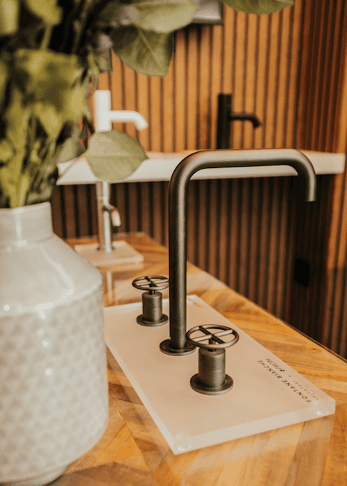 Modern black kitchen tap with dual handles on wooden countertop.