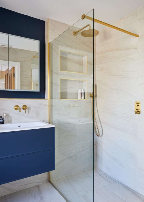 Modern bathroom with blue vanity, gold fixtures, and walk-in shower with glass partition.