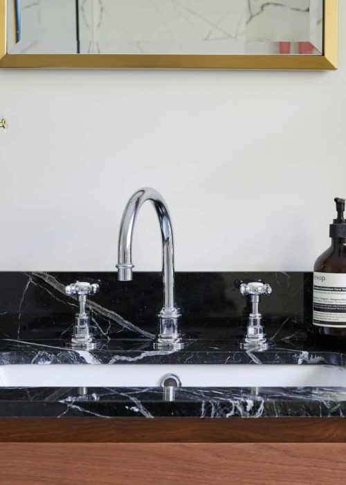A modern bathroom sink with a black marble counter, featuring a mirror, electric toothbrush, soap dispenser, candle, and flowers in a vase.