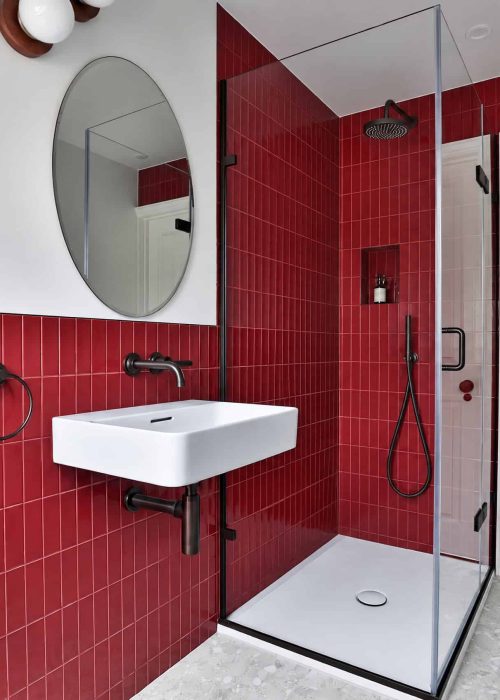 Modern bathroom with red tiled shower area and white sink.