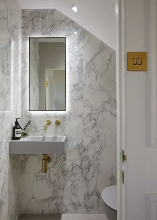Modern marble bathroom with sleek sink, mirror, and gold fixtures.