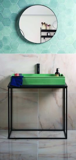 Green sink on a black stand with blue towel, hexagonal tile wall, and circular mirror reflecting shelves with toiletries.