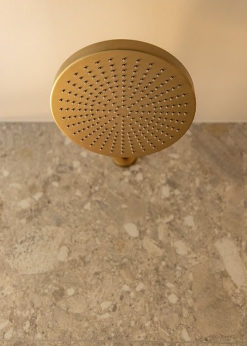 Close-up of a gold shower head above a stone bathroom surface.