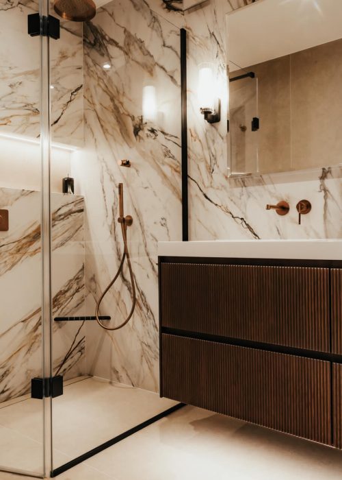 Luxurious bathroom with marble walls, glass shower, wooden cabinet, and warm lighting. Sophisticated and serene atmosphere.