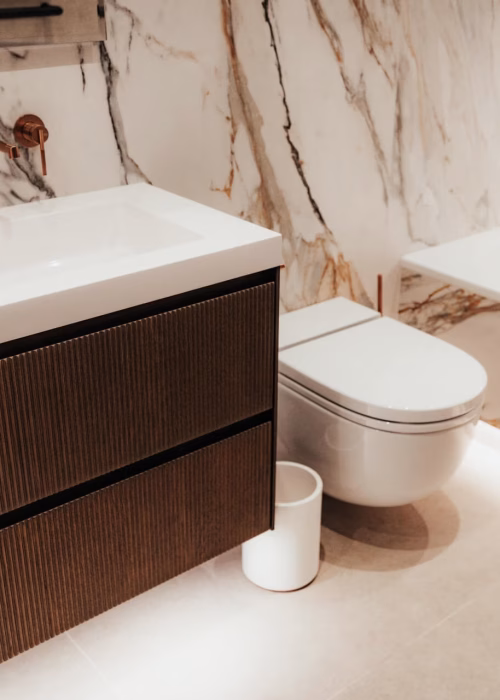 Luxurious bathroom with marble walls, modern vanity with dual sinks, copper faucets, and an integrated toilet. Soft lighting creates a warm ambiance.