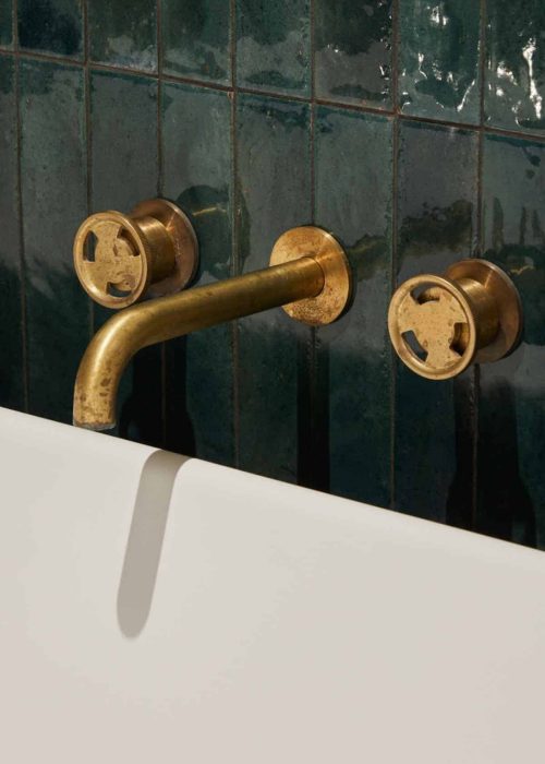 Close-up of vintage brass bathroom tap and wall-mounted fixtures with green tiles.