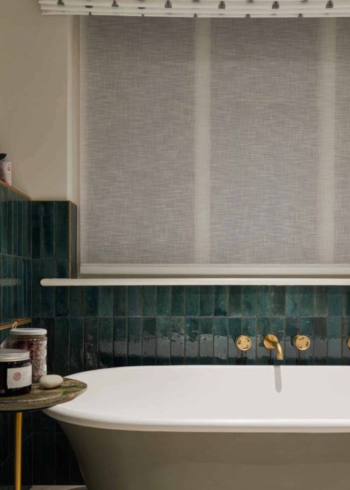 Modern bathroom with grey roller blind and green tiled wall behind a white bathtub.
