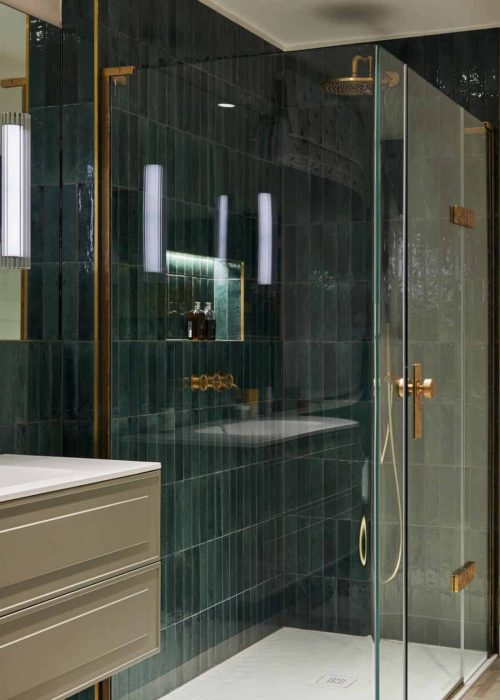 Modern bathroom with dark green tiles and gold fixtures in a glass shower enclosure.