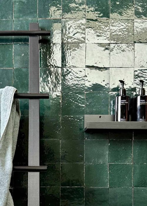 Green coloured bathroom tiles with a shelf and toiletries for luxury bathroom design.