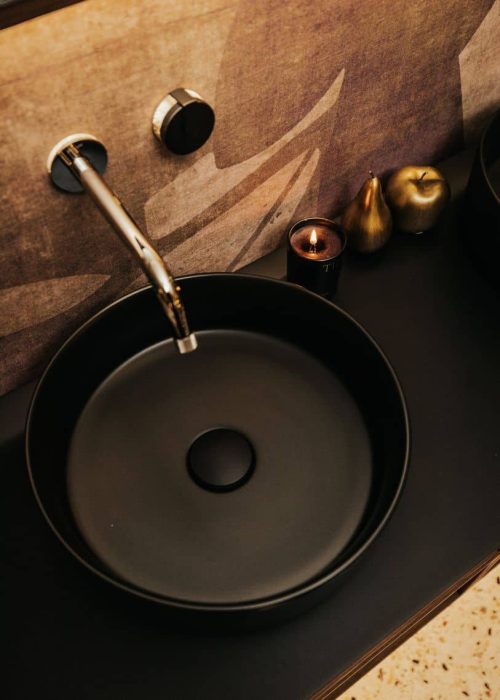 Modern black bathroom sink with gold and black accessories and candles.