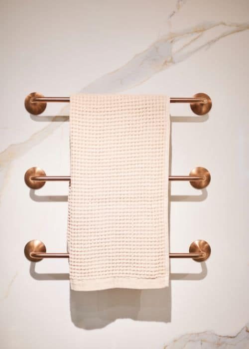 Elegant beige towel on copper towel rail in modern bathroom setting.