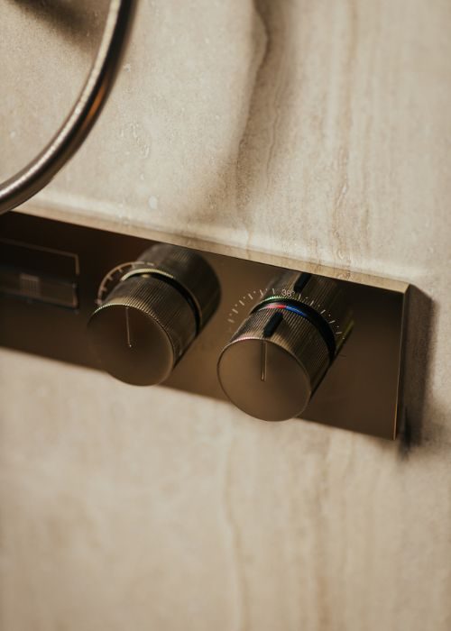 Close-up of bathroom radiator control knobs on a tiled wall.
