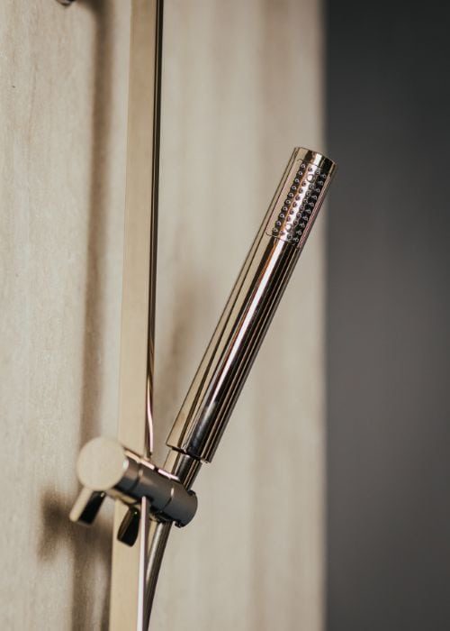 Modern chrome handheld shower head mounted on wooden wall in bathroom.