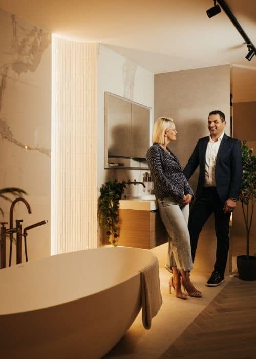 Two professionals discussing bathroom design in a modern showroom with a bathtub and TV.