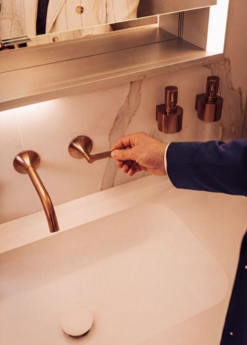 Close-up of a person turning on a modern copper bathroom tap in a stylish bathroom.