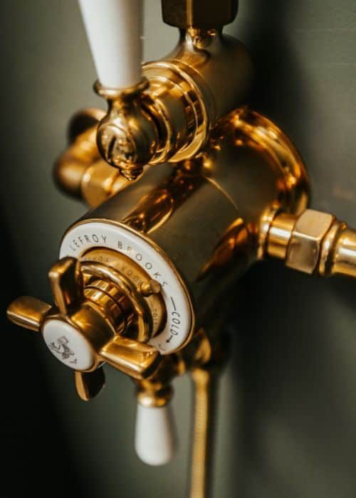Close-up of a polished gold radiator valve with white handle and white pipe.