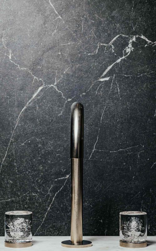 Modern black marble bathroom wall with sleek silver tap and glasses.