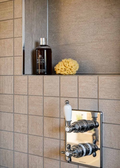 Modern shower panel with chrome controls and a beige tiled wall in bathroom.