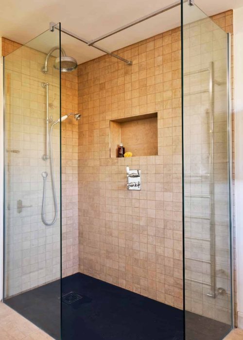 Modern walk-in shower with beige tiles and glass enclosure in bathroom.