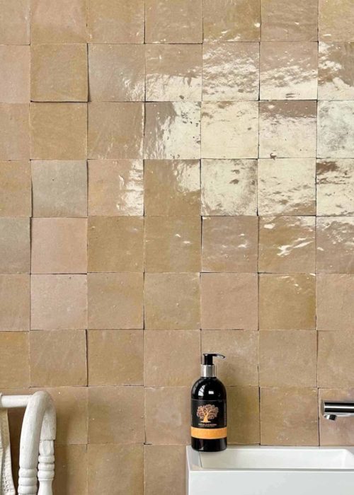 Beige glossy square bathroom tiles with a white sink and black soap dispenser.