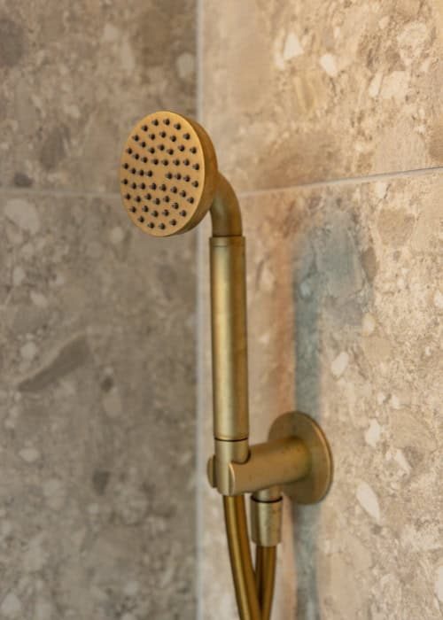 Brass shower head and arm mounted on a tiled bathroom wall.