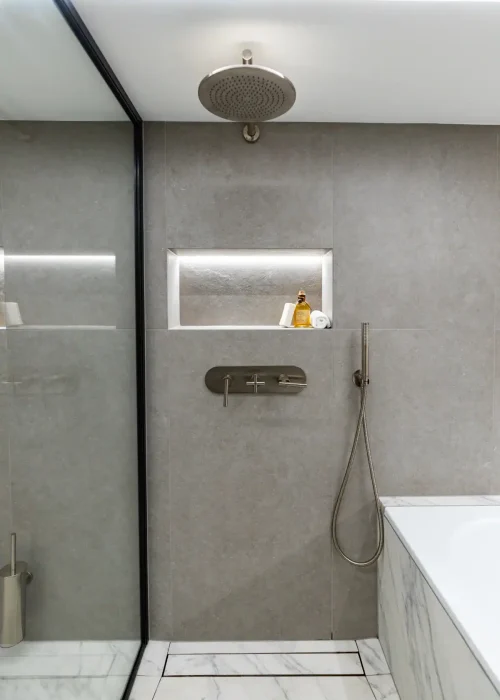 Modern walk-in shower with rain shower head and built-in niche in grey tiled bathroom.