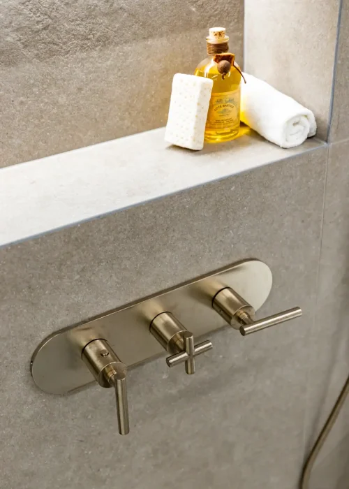 Modern bathroom shower controls with soap and towel on shelf.