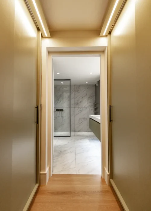 Modern master bathroom with marble walls and walk-in shower seen through doorway.