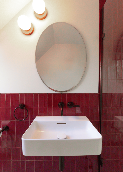 Modern white bathroom sink with red tiled wall and oval mirror.