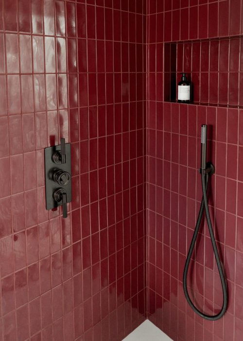 Modern red tiled shower with handheld showerhead and built-in shelf.