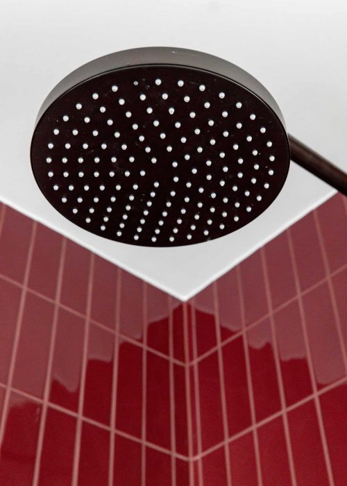 Modern black rain shower head with red tiled bathroom ceiling.