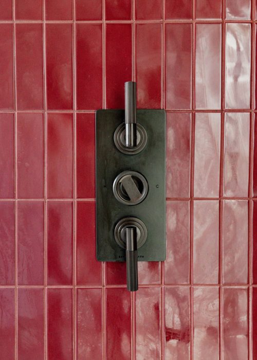 Close-up of vintage shower control with red tiled wall in bathroom.