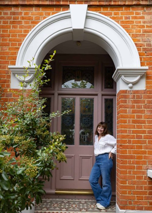 Woman leaning against a Victorian-style front door with brickwork and decorative arch.